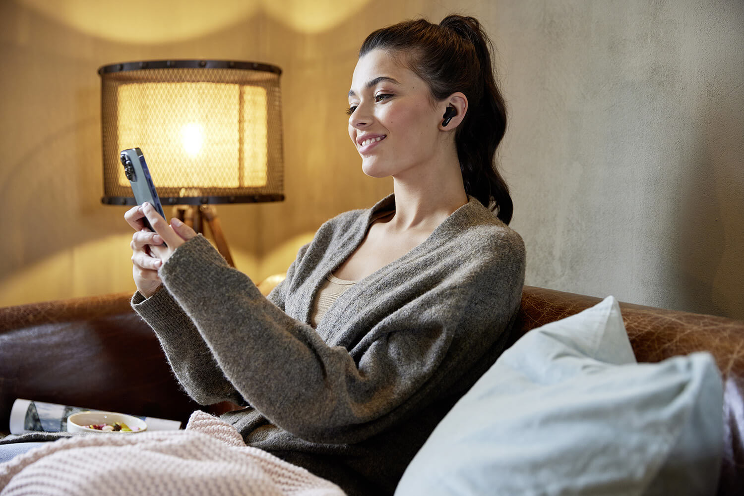 Entspannte Frau auf dem Sofa mit Handy und den Intenso Buds.